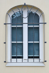 An arched window with a black metal grate on a yellow wall