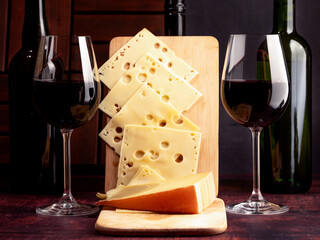 A stylized antique still life with glasses of wine, cheese and three wine bottles.