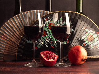 Still life with a glass of wine, bottles of wine, a pomegranate and a fan. Italian, French and Spanish motives.