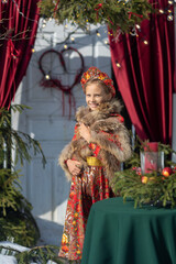 A blonde girl in a national Russian costume on the Maslenitsa holiday. A child in a traditional costume with fur trim and a headdress against a festive backdrop. Winter scene with a beautiful girl