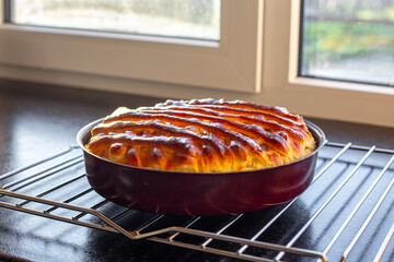 A rich pie with jam, the top crust is made of woven dough in a lattice pattern. Delicious pastries on the kitchen countertop near the window