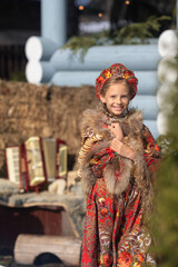 A blonde girl in a national Russian costume on the Maslenitsa holiday. A beautiful russian girl in a national costume made of a fur cape and kokoshnik on the background of a hayloft. 