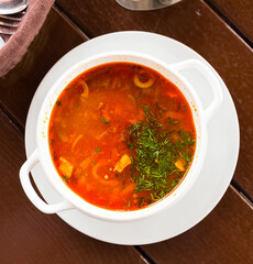 Delicious solyanka on broth with meat, olives and pickled cucumbers served with fresh herbs