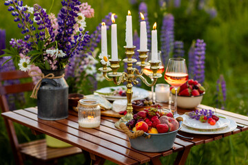 Perfect surprise date for loving couple, private wedding, romantic marriage proposal. Summer, sunset, golden hour. Appetisers. Beautiful elegant outdoor arrangement in meadow with purple blue lupins