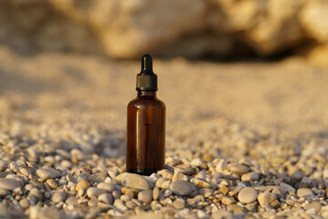 brown mockup of glass jar of serum with dropper on small pebble on the background of rock on beach. Concept of natural cosmetics for face care, wrinkle reduction, moisturizing. Image for your design
