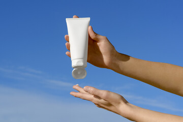 Female hands squeeze white mock-up tube of cream onto finger on blue sky background. Concept of...