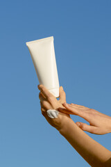 Vertical image of a female hand applying a sample of cream and holding a white mockup tube of...