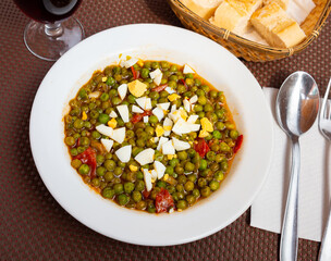 Guisantes a la Murciana - Peas Murcia Style. Juicy peas sauteed with cured ham served with boiled egg on white plate, popular