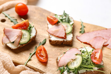 Wooden board of delicious sandwiches with cream cheese, ham and vegetables, closeup