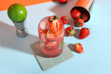Glass of fresh strawberry mojito with jigger and shaker on blue table near orange wall