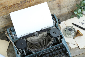 Vintage typewriter, inkwell, sheets and houseplant on brown wooden background