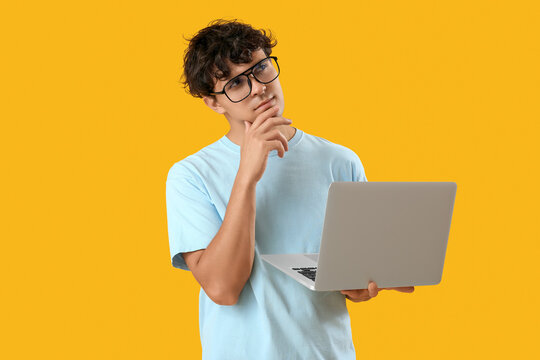 Thoughtful male programmer with laptop on orange background