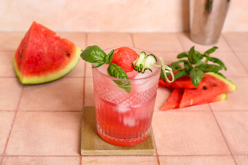 Glass of tasty watermelon cocktail with shaker and mint on tile table near grunge pink wall
