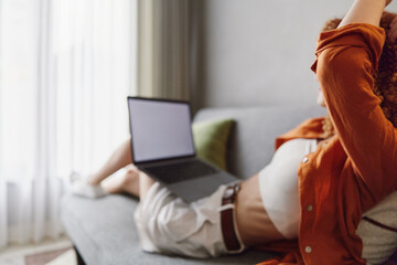 A relaxed woman enjoying her time on a laptop in casual summer clothes, sitting on a couch with soft lighting and a cozy atmosphere
