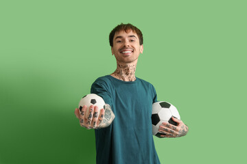 Happy young man with soccer balls on green background