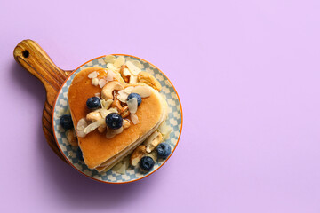 Plate with tasty pancakes in shape of heart, blueberry and nuts on purple background. Valentine's Day celebration