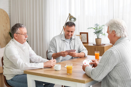 Elderly men with drinks playing cards at home