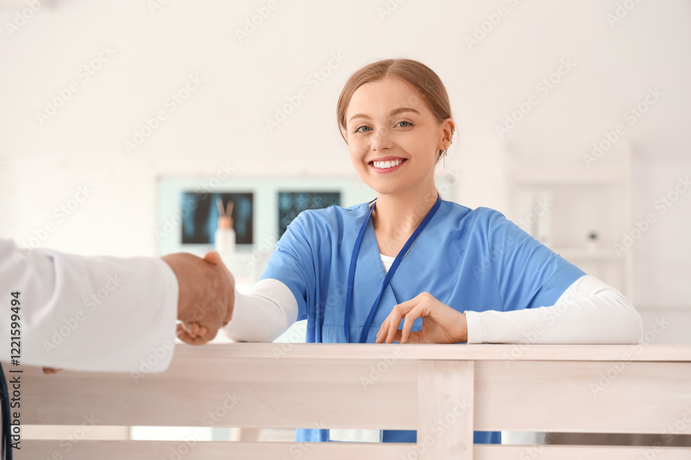 Wall mural Female nurse with doctor shaking hands at reception in clinic