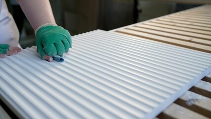 Manufacturing process of sanding a white wooden panel with parallel grooves, performed by a worker...