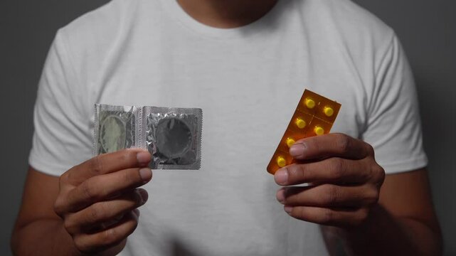 Man showing condom and medicine pack on gray background