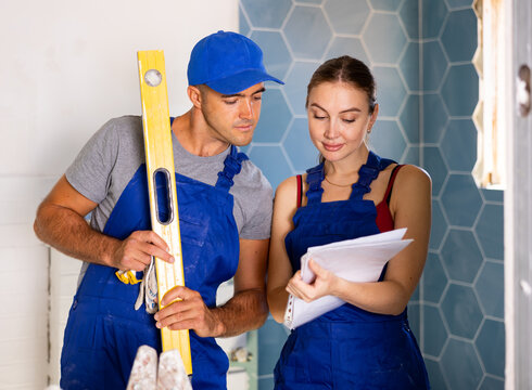 Caucasian man and woman in overalls discussing project documentation of bathroom design.