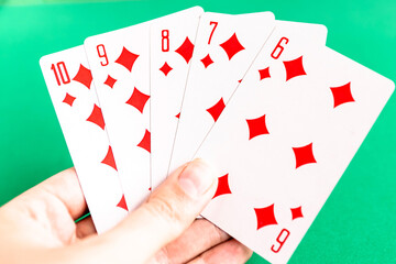 Poker straight flush playing card in woman’s hand, green background