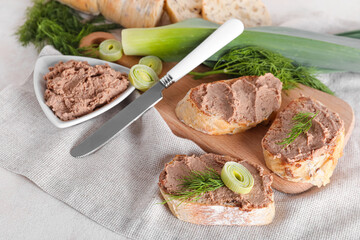 Wooden board with toasts, tasty pate, dill and green onion on light background