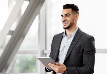 Portrait Of Handsome Middle Eastern Businessman Using Digital Tablet While Waiting For Flight At Airport Terminal, Smiling Arab Man In Suit Holding Tab Computer And Looking Away, Copy Space