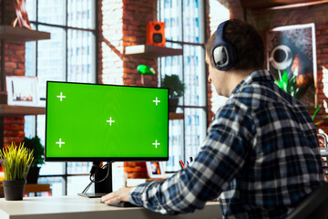 Worker wearing headphones engaging in online training session on chroma key PC, navigating course...