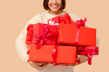 Beautiful young woman with gift boxes on beige background. Valentine's Day celebration