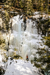A man is standing on a snow-covered cliff, looking down at the ice below
