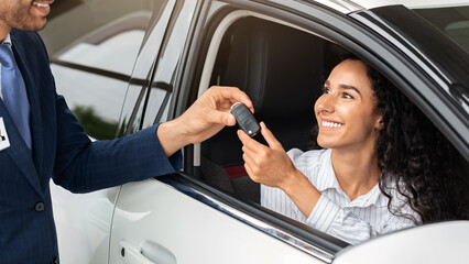 Happy business woman buying new luxury auto in new showroom, taking car key from middle-eastern man sales assistant and smiling, closeup. Car purchasing, automobile leasing concept