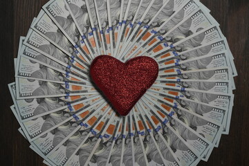 A circle made from american hundred dollar bills with a red heart shape in the center, closeup, top view