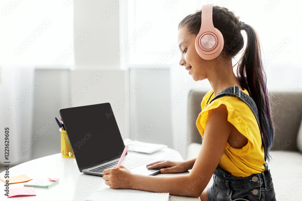 Aufkleber side view profile portrait of girl in pink headset doing homework, sitting on couch at table using l