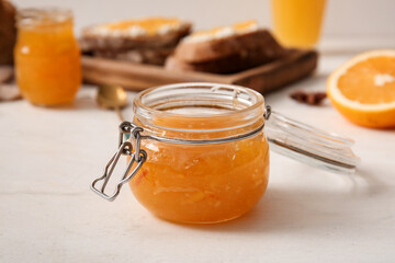 Jar of tasty orange jam on white wooden background