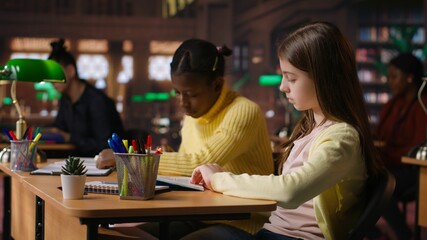 Teen girls reading books in the library to focus on mandatory literature and gaining knowledge for academic curriculum during study time. Young scholars focusing on lecture tasks. Camera B.