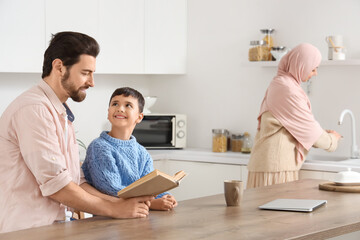 Happy Muslim father with his son reading book in kitchen