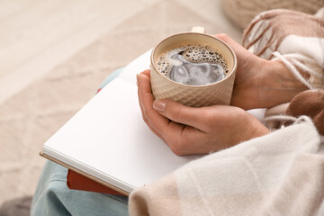Young woman with books, blanket and cup of coffee sitting on armchair at home, closeup