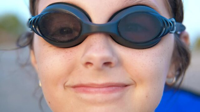 Young swimmer girl putting swimming goggles on. Portrait features a smiling caucasian teenager girl with freckles, happily putting on her swimming goggles.