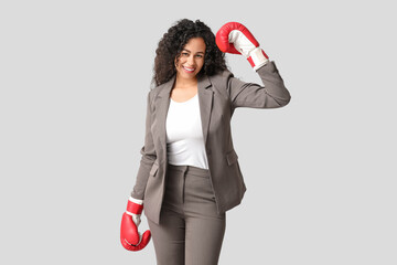 Young African-American businesswoman with boxing gloves on light background. Knockout concept