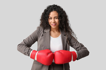 Young African-American businesswoman with boxing gloves on light background. Knockout concept