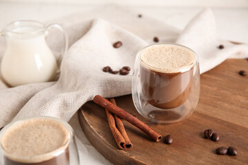 Glasses of hot coffee with cinnamon and jug of fresh milk on white background