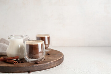Glasses of hot coffee with cinnamon and jug of fresh milk on white background