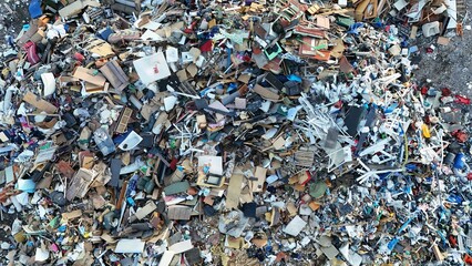 Aerial view of a dense pile of discarded furniture, plastic, and waste materials in a landfill. The...