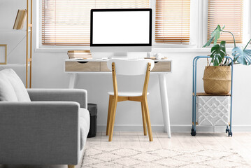 Workplace with blank computer monitor near window in light room interior