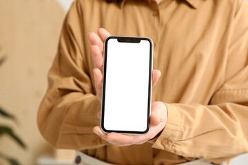 Young woman holding blank mobile phone at home, closeup