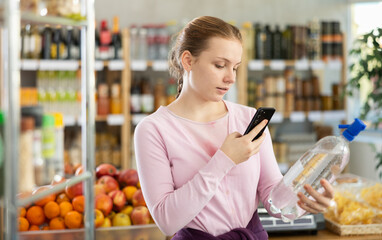 Female buyer checks suitability - scans QR code on bottle of water label in a grocery store