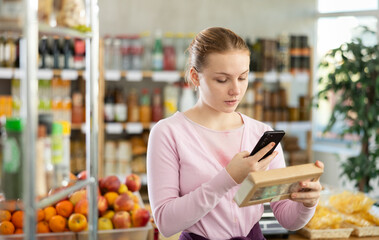 Female shopper scanning QR code on sweet cookies label in grocery department of supermarket
