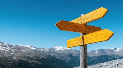 A wooden signpost with yellow arrows against a clear blue sky and mountain backdrop.