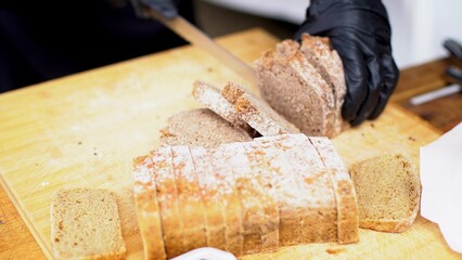 a man's hand in a glove holding a knife and cutting bread
